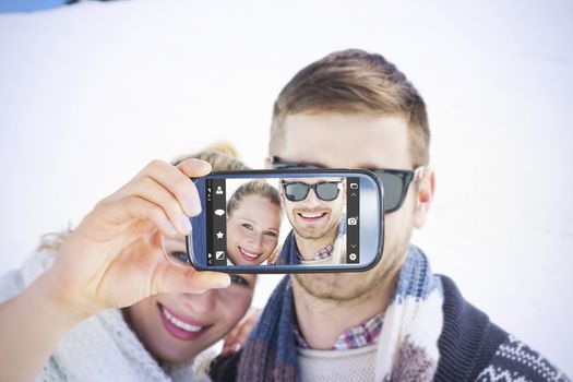 Hand holding smartphone showing against smiling couple in front of snowed hill