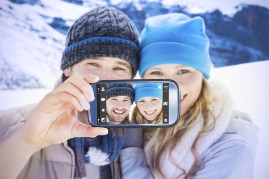 Hand holding smartphone showing against couple in warm clothing on snow covered landscape