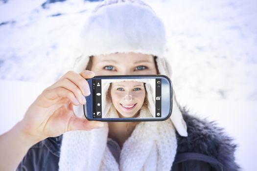 Hand holding smartphone showing against woman in warm clothing on snow covered landscape