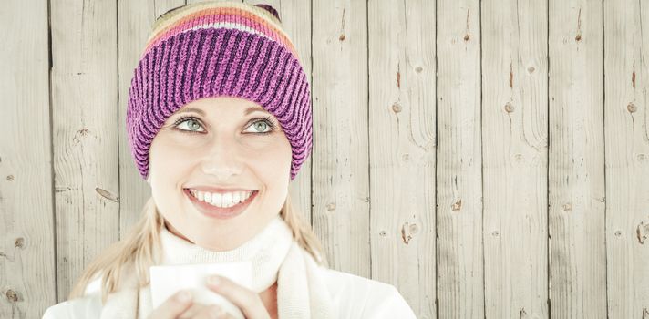 Smiling woman with a colorful hat and a cup in her hands against wooden background