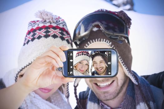 Hand holding smartphone showing against smiling couple in woolen hats on snow covered landscape