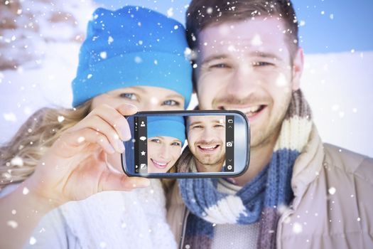 Hand holding smartphone showing against couple in warm clothing on snow covered landscape