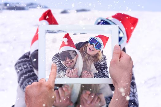 Hand holding tablet pc against close up of a cheerful couple in ski goggles on snow