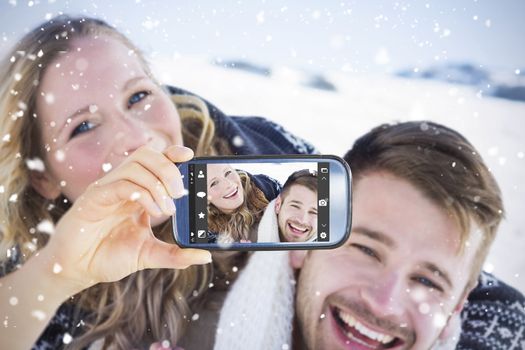 Hand holding smartphone showing against close up of a cheerful couple holding hands on snow