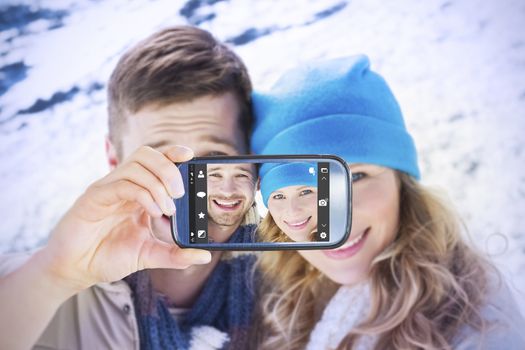 Hand holding smartphone showing against loving couple in warm clothing on snow covered landscape