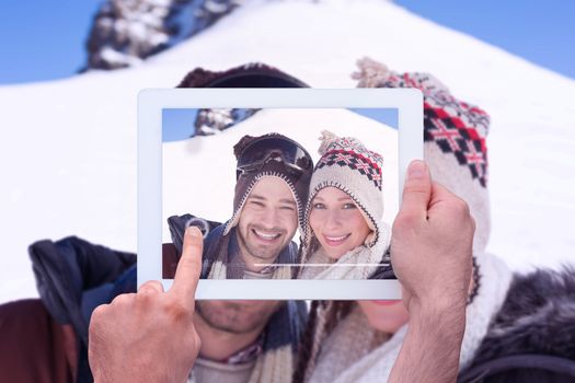 Hand holding tablet pc against close up portrait of a smiling couple in woolen hats