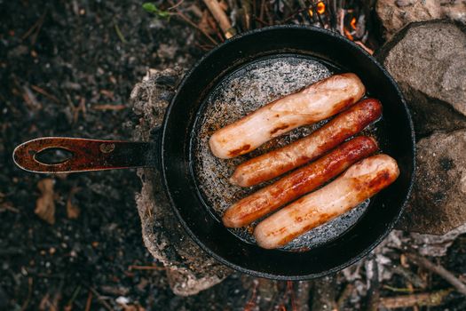 Roasting sausages in a frying pan over an open fire. Preparing food in nature. Lunch in the open air. Picnic in the forest. Food on fire