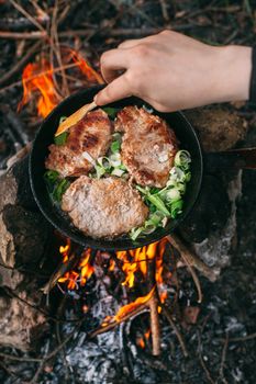 Frying meat in a pan over an open fire with leek. Steak in a pan on a fire. Cooking in nature. Picnic. Grill on fire. Hand with a wooden spatula.