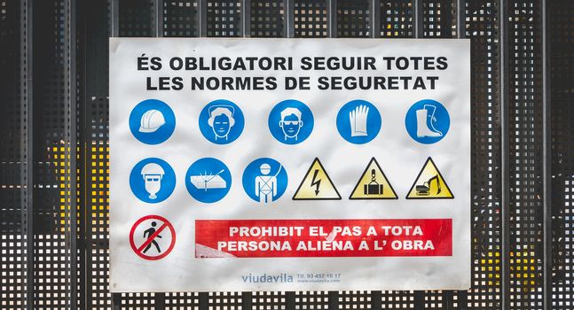 Barcelona, Spain - June 21, 2017: at the entrance to a construction site, sign written in Catalan - it is mandatory to comply with all safety rules (es obligatori seguir totes les standards de seguretat)