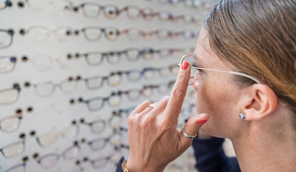woman chooses and tries glasses in optics store