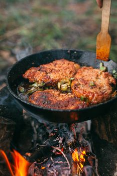 Frying meat in a pan over an open fire with leek. Steak in a pan on a fire. Cooking in nature. Picnic. Grill on fire. Hand with a wooden spatula.