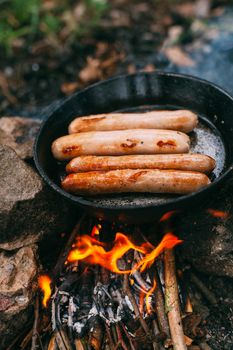 Roasting sausages in a frying pan over an open fire. Preparing food in nature. Lunch in the open air. Picnic in the forest. Food on fire