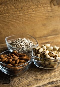 Almond, pistachio and sunflower seeds in a small plates which standing on a wooden vintage table. Nuts is a healthy vegetarian protein and nutritious food. Nuts on rustic old wood