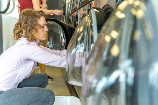 woman pulling clothes out of automatic washing machine in public laundry.