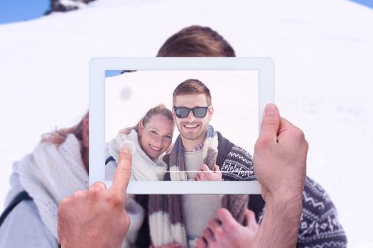 Hand holding tablet pc against smiling couple in front of snowed hill