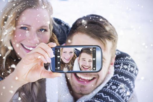 Hand holding smartphone showing against close up of a cheerful couple holding hands on snow