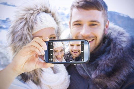 Hand holding smartphone showing against loving couple in jackets against snowed mountain