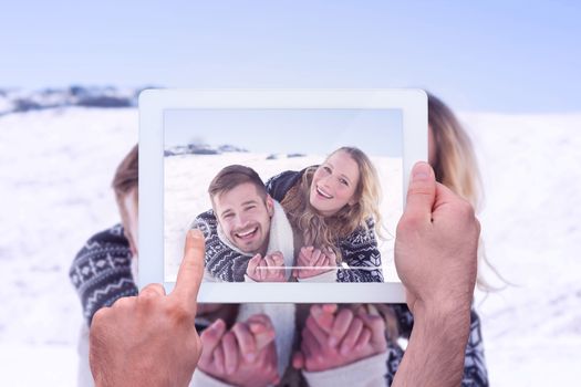 Hand holding tablet pc against close up of a cheerful couple holding hands on snow