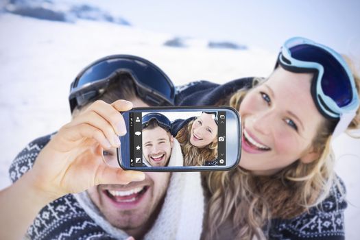 Hand holding smartphone showing against cheerful couple with ski goggles on snow