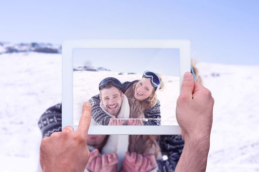 Hand holding tablet pc against cheerful couple with ski goggles on snow