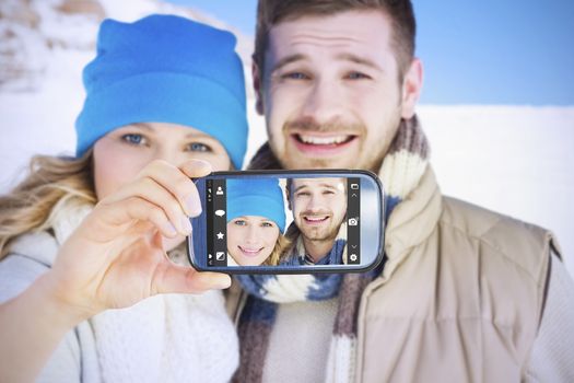 Hand holding smartphone showing against couple in warm clothing on snow covered landscape