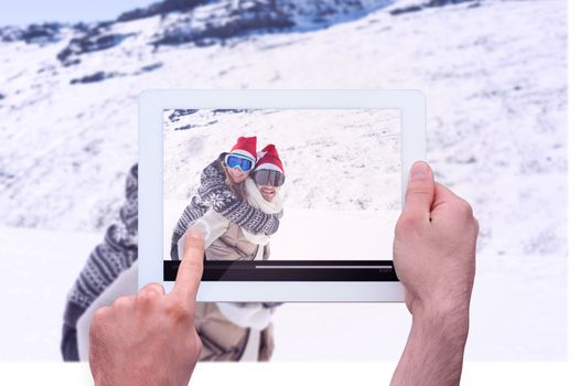 Hand holding tablet pc against man piggybacking cheerful woman on snow