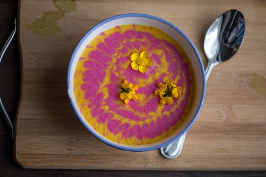 Vegetarian cream pumpkin and beet mix soup decorated with fresh yellow flowers delicious and healthy food