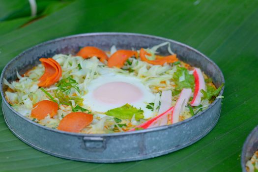 Delicious egg pan with sausage ,crab stick, cabbage and lettuce in small metal pan on green banana leave. Healthy breakfast in morning.