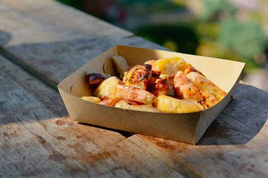 Grilled banana with coconut sauce in brown paper plate on wooden table with sun light. Reduce plastic and foam container.