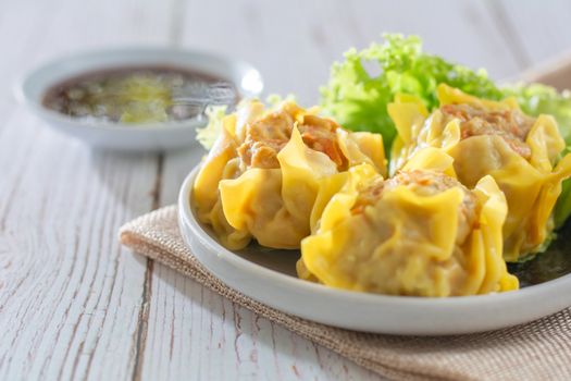 Chinese Steamed Dumpling, Shumai on white dish served with soy sauce and 
lettuce leaves on brown cloth and wooden table. Delicious Dimsum pork.