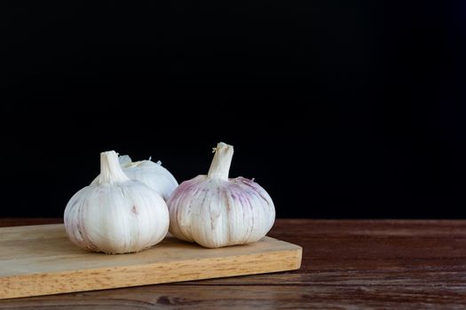 Group of garlic on chopping board and wooden table with black background. Copy space for your text.