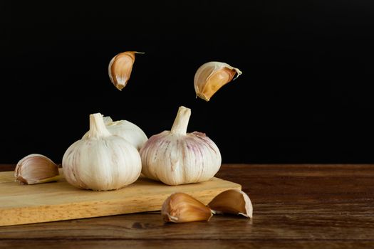 Group of garlic on chopping board and some garlic cloves floating in the air on wooden table with black background. Copy space for your text.