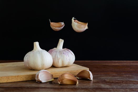 Group of garlic on chopping board and some garlic cloves floating in the air on wooden table with black background. Copy space for your text.