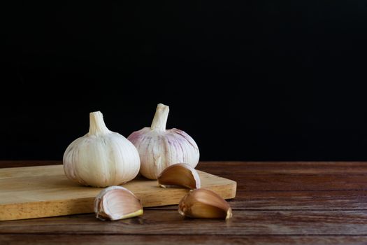 Group of garlic on chopping board and wooden table with black background. Copy space for your text.