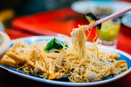 Delicious Chinese food. Eatting stir fried noodle and shiitake with chopsticks serve in restaurant at china town in Thailand. Selective focusing.