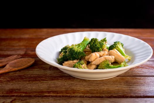 Stir fried broccoli and chicken in white plate on wooden table.