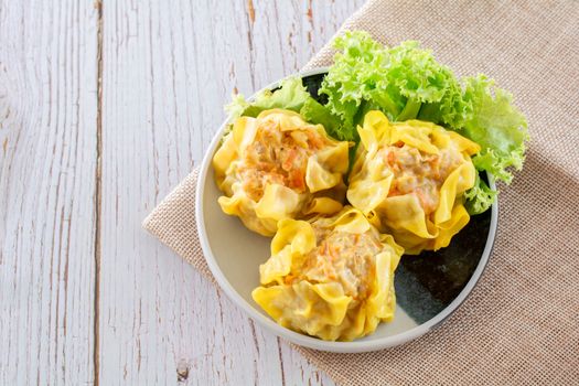 Chinese Steamed Dumpling, Shumai on white dish served with soy sauce and 
lettuce leaves on brown cloth and wooden table. Delicious Dimsum pork.