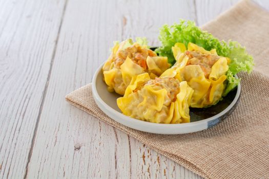 Chinese Steamed Dumpling, Shumai on white dish served with soy sauce and 
lettuce leaves on brown cloth and wooden table. Delicious Dimsum pork.