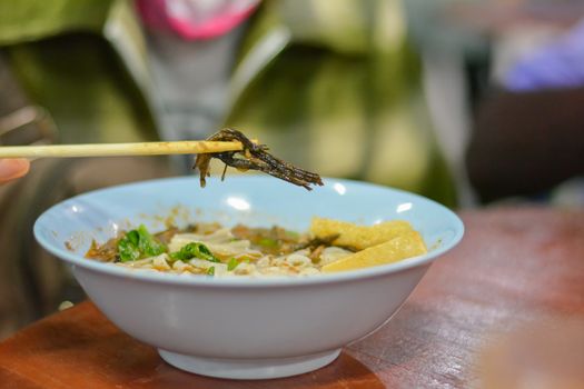 Thai local food Northen of Thailand. Eattind rice noodles with spicy pork sauce with chopsticks. Selective focus.