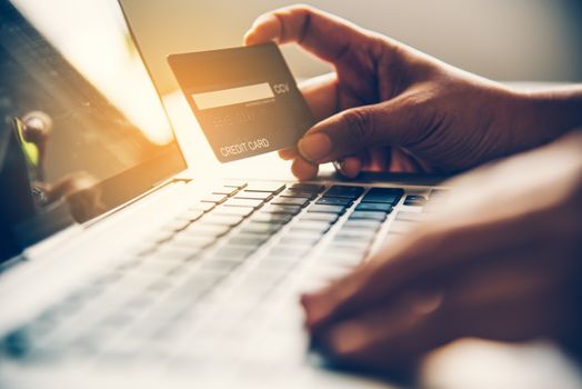 Hand holding a credit card in their hands and find information about a product using their mobile device to make purchases online and conduct financial transactions.