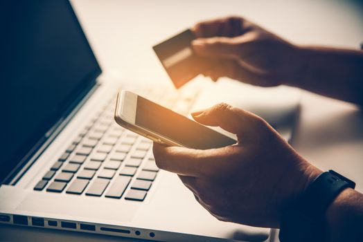 Hand holding a credit card in their hands and find information about a product using their mobile device to make purchases online and conduct financial transactions.