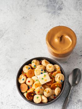 Mini pancakes cereal and dalgona coffee on gray cement background, copy space. Trendy food and drink - tiny panckakes and whipped instant coffee with milk or korean dalgona coffee. Top view. Vertical