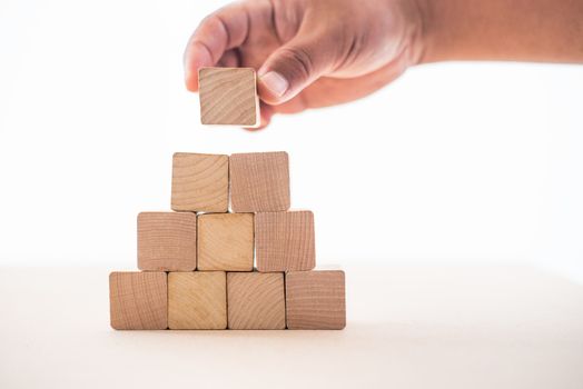 The hand of the businessman caught the wooden blocks placed on a white background as a house to show the stability of doing business.