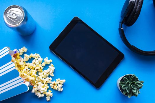 A tablet on a blue background with popcorn and headphones