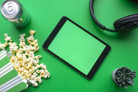 A tablet on a green background with popcorn and headphones