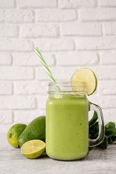 Avocado, lime and spinach smoothie in mason jar decorated with a slice of lime front view on white brick wall background