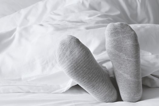 foot in gray socks relaxing on the white bed