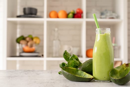 Avocado, lime and spinach smoothie in glass bottle front view on home kitchen background with copy space