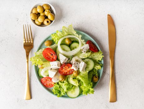 Healthy food. Top view of greek salad with olives and fresh vegetables on blue plate with golden knife and fork