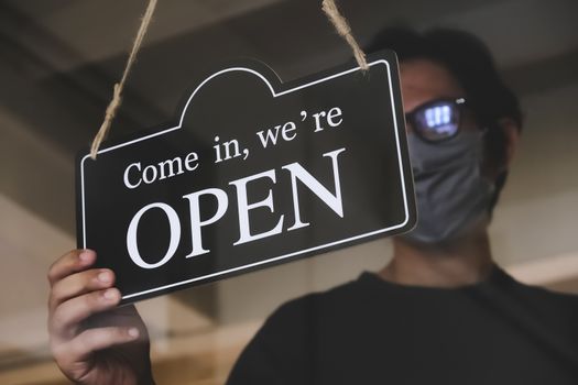 the state allows retail stores or restaurants and businesses to reopen after coronavirus restrictions. man with face mask turning a sign on a door shop. economy starts running after being on lockdown.